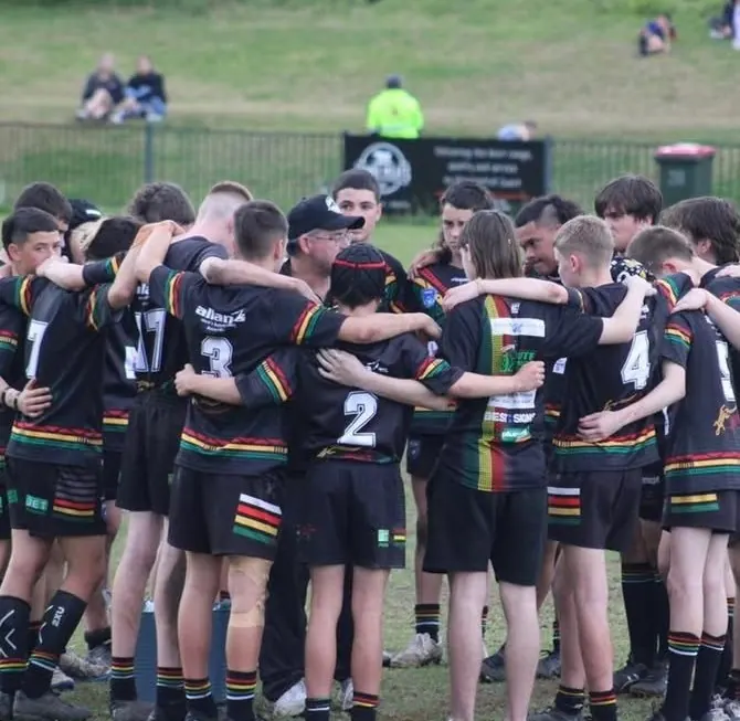 A junior Panthers team in a tight huddle on the field with their coach before a game