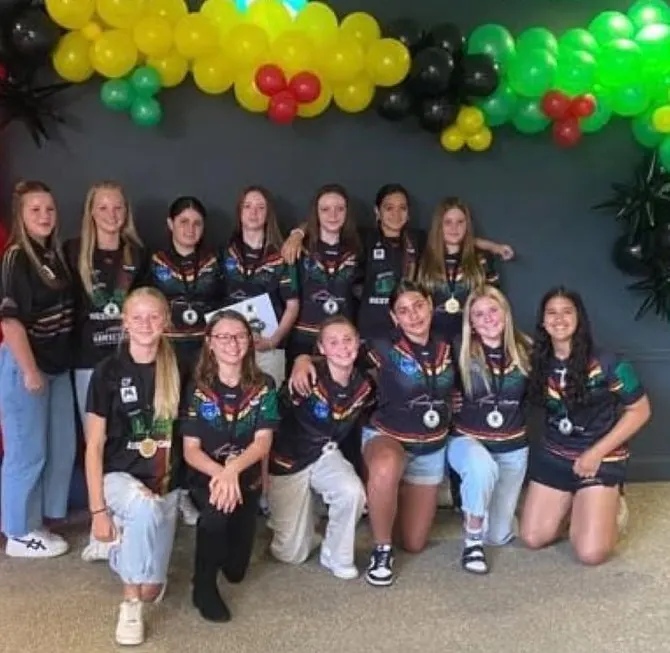 A Panthers girls team in jerseys and medals poses under green, gold and black balloons at presentation night